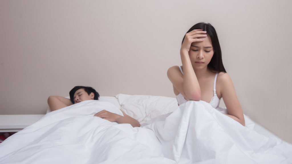 Un hombre duerme en la cama mientras la mujer se preocupa